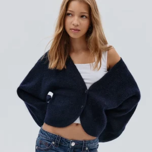 Mörkblå bolero - Säljer en mörkblå  bolerokofta med vida ärmar och knäppning framtill. Koftan är stickad och har en croppad passform som ger en cool och avslappnad look. Perfekt att slänga över ett linne eller t-shirt. Använd fåtal gånger och är i princip helt ny.