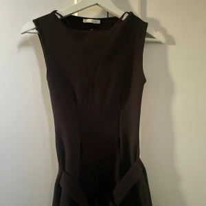 Brun ärmlös klänning med bälte - Stilren brun klänning från Zara med ärmlös design och rund halsringning. Klänningen har ett brett tygbälte i midjan som är en snygg detalj. Tajt stretchigt tyg!
