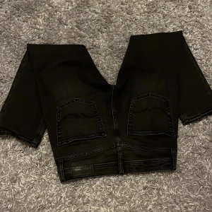 Svarta jeans från Jack & Jones - Svarta jeans från Jack & Jones, modell Comfort/Mike. Jeansen har klassisk femficksdesign, raka ben och diskreta sömmar. Materialet är jeans och färgen är helsvart, vilket gör dem enkla att matcha med olika outfits. Passar runt 175, slim modell