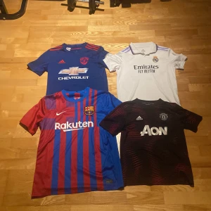 Fotbollströjor - Säljer fyra snygga fotbollströjor: FC Barcelona (röd/blå randig, Nike), Manchester United (blå med röda detaljer, Adidas), Manchester United (svart med röda detaljer, Adidas) och Real Madrid (vit med lila detaljer, Adidas). Alla är kortärmade och har klubbmärken och sponsorer tryckta på bröstet.