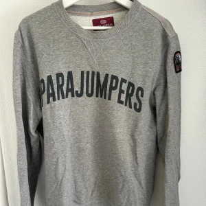 Grå fleece-tröja från Parajumpers - Grå långärmad fleece-tröja från Parajumpers med stor logga över bröstet och patch på ärmen.  Nypris 2500kr