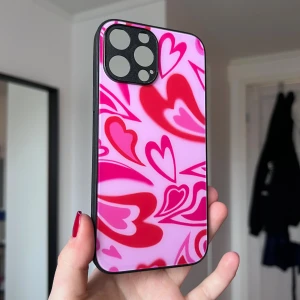 Mobilskal med rosa hjärtan - Ett mobilskal till iPhone 13 Pro Max med rosa bakgrund samt röda och rosa hjärtan. Svarta kanter. Sparsamt använt.