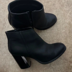 Svarta stövletter med klack - Snygga svarta stövletter med chunky klack och rund tå. Skorna är i skinnimitation och har en stilren design som passar till många outfits. Perfekta för dig som vill ha en klassisk men trendig look.