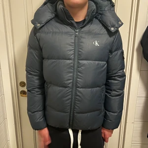 Mörkblå pufferjacka Calvin Klein Jeans - Tja! säljer denna Snygga mörkblåa pufferjacka från Calvin Klein Jeans Pga att den är för liten för mig bara använd i vintras. Jag är 180 på bilden så skulle säga att den passar om man e lite kortare, hör av er om ni har fler frågor 