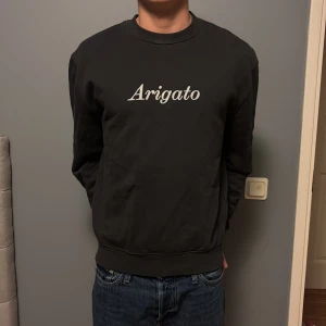Grå sweatshirt Axel Arigato - Grå sweatshirt från Axel Arigato med vit 'Arigato'-text på bröstet. Klassisk rund halsringning och ribbade muddar vid ärmslut och nederkant. Tillverkad i mjuk bomull, perfekt för en clean och stilren look. Nypris 1399kr mitt pris 499