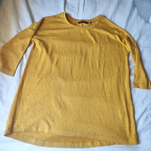 Gul tröja från KappAhl med trekvartsärm - Snygg gul tröja från KappAhl i mjukt material. Modellen har rund halsringning och trekvartsärmar, perfekt för lager på lager eller som den är. Enkel och stilren design som passar till många outfits.