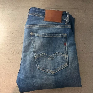  Replay Rocco jeans  - Snygga blå jeans från Replay, modell Rocco med comfort fit. Klassisk femficksdesign, ljus tvätt och detaljerade sömmar på bakfickan. Märkespatch i läder baktill och diskret Replay-logga vid fickan. Perfekta för en avslappnad och trendig look. 