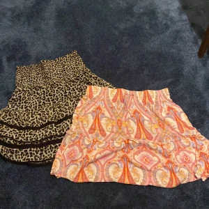 Två korta kjolar, leopard & paisley - Säljer två snygga kortkjolar! Ena är från Lindex med leopardmönster i beige och svart, smock i midjan och volangdetaljer. Den andra har paisleyinspirerat mönster i orange, rosa och lila toner, med lätt volang. Perfekta för dig som gillar färg och mönster. Dem kommer tillsammas! ❤️