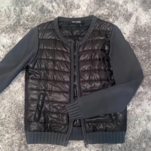 Svart quiltad pufferjacka från top secret  - Snygg svart pufferjacka från The Kooples med quiltad framsida och släta ärmar. Jackan har ribbade muddar, rund halsringning och dragkedja framtill. Perfekt för dig som gillar en stilren look med sportig touch. 