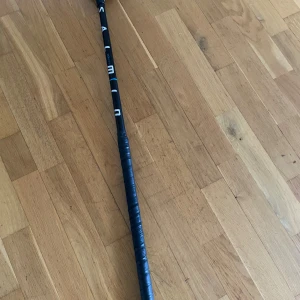 Salming composite material flex 27  - Bilderna visar en innebandyklubba från märket Salming, modell Composite. Med klubban för man ett bättre dragskott med den lila inåt böjen. Klubban har ett svart och blått skaft med tydlig Salming-logga och ett grepp i gott skick. Bladet är svart och ser ut att vara i bra skick utan synliga sprickor eller större slitage. Perfekt för både träning och match. Pris kan diskuteras 