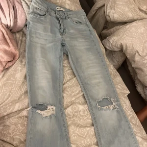 Ljusblå bootcut jeans med slitningar - Säljer ett par ljusblå bootcut jeans från Gina Tricot med snygga slitningar på båda knäna. Jeansen har klassisk femficksdesign, normal midja och vida ben. Perfekta för dig som gillar en avslappnad och trendig look.