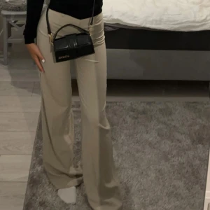 Beiga vida kostymbyxor - Snygga beiga kostymbyxor med hög midja och vida ben. Byxorna har klassiska hällor för bälte och stängs med dragkedja och knapp. Perfekta för en clean och stilren look. Materialet känns mjukt och följsamt.