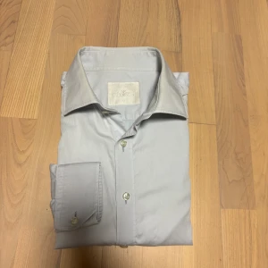  Skjorta från Oscar Jacobson - Snygg ljusgrå skjorta från Oscar Jacobson i klassisk modell.  Observera att det finns vissa missfärgningar vid armhålorna och kragen. Hör gärna av dig vid frågor, mått eller om du vill ha fler bilder.