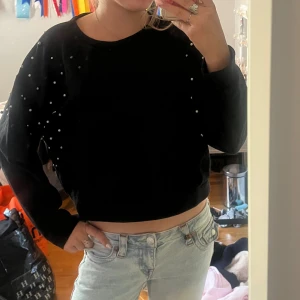 Svart sweatshirt med pärlor från Amisu - Svart sweatshirt från Amisu med pärldetaljer på axlar och ärmar. Tröjan har en croppad passform och långa ärmar. Perfekt för dig som vill ha något basic men ändå med en twist. Superenkel att styla till jeans eller kjol. Jag brukar ha xs s och den här passar mig 