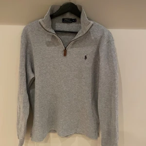 Grå half zip tröja från Polo Ralph Lauren - Klassisk grå långärmad tröja från Polo Ralph Lauren med half zip och broderad logga på bröstet. 