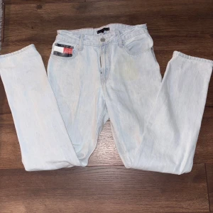Ljusblå jeans från Tommy Hilfiger - Säljer ett par ljusblå jeans från Tommy Hilfiger med klassisk femficksdesign och raka ben. Jeansen har snygga detaljer med Hilfiger-logga på bakfickan och vid linningen samt en liten röd, vit och blå detalj på myntfickan. Perfekta för en avslappnad stil.