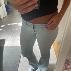 Ljusblå bootcut jeans låg midja - Säljer ett par ljusblå jeans med bootcut-modell och låg midja. Jeansen har klassisk femficksdesign, dragkedja och knapp framtill. Snygg passform som sitter tajt upptill och släpper ut vid bensluten. Perfekta för dig som gillar en retro vibe.