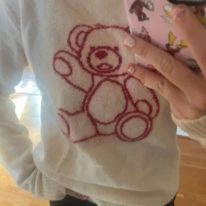 Vit stickad tröja med nalle från Brandy Melville - Supergullig vit stickad tröja från Brandy Melville med ett stort rött nalletryck på bröstet. Tröjan har rund halsringning, långa ärmar och ribbade muddar. Perfekt för dig som gillar söta detaljer och vill ha en mysig look. Använd en gång.