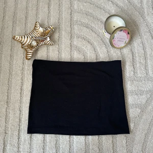 Svart top med mini tjol - Säljer en stilren svart top med enkel bandeau-underdel och trekantsformad överdel med smala axelband. Båda delarna är enfärgade och har en klassisk, tidlös look. Perfekt för strandhäng eller poolparty i sommar!