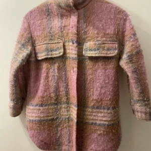 Rutig overshirt från Zara i rosa och beige - Säljer en fluffig och mysig overshirt från Zara i storlek 140. Jackan har ett rutigt mönster i rosa, beige och inslag av blått, med två stora bröstfickor och knappar framtill. Perfekt för lager-på-lager och chill stil.