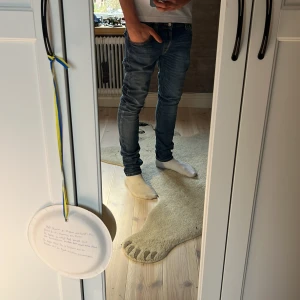 Blå jeans från Nudie - Snygga blå jeans från Nudie med slim/skinny passform och klassisk femficksdesign. Jeansen har en mörk tvätt med slitningar och kontrastsömmar, samt Nudie-logga på bakfickan. Perfekt för dig som gillar en smal siluett och stilren look.