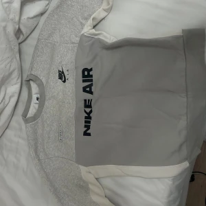 Nike Air grå sweatshirt med logga - Snygg grå Nike Air sweatshirt med stora svarta loggor både fram och bak. Tröjan har rund hals, långa ärmar och är gjord i mjuk bomullsblandning. Färgblock i ljusgrått och vitt ger en sportig vibe. Perfekt för dig som gillar streetwear och sportig stil.(pris kan diskuteras vid snabb affär)