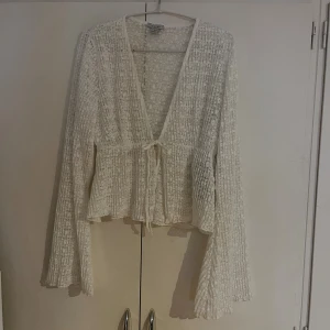 Vit spetsig blus från Amisu - Säljer en vit blus från Amisu i storlek M. Blusen är gjord i spets med ribbad struktur, har långa ärmar och en v-ringad omlottfront med knyt i midjan. Den är lätt transparent och har en flowy, feminin siluett som ger en romantisk vibe.