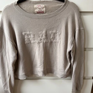 Beige sweatshirt från Pull&Bear - Säljer en beige sweatshirt från Pull&Bear med broderad text 'RAD' framtill. Tröjan har en loose passform, ribbade muddar och är långärmad. Tröjan är något urtvättad och nopprig, se bilder. 