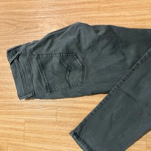 Replay Anbass jeans grå storlek 34 - Snygga Replay Anbass jeans i grått med klassisk femficksdesign och raka ben. Jeansen har diskreta sömmar på bakfickorna och en svart Replay-lapp vid midjan. Perfekt passform och stilren look för dig som gillar streetwear.