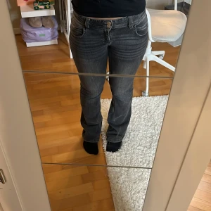 Svarta bootcut jeans med låg midja - Säljer ett par svarta jeans med snygg bootcut och låg midja. Jeansen har klassiska fem fickor, dragkedja och 2 knappar framtill. Materialet har stretch och färgen är en svart tvätt som ger en cool vibe. Perfekta för dig som gillar en avslappnad men trendig look. Storlek 164 men sitter som xs-m