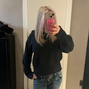 Svart stickad hoodie med huva - Säljer en svart stickad hoodie med huva och snörning. Tröjan har långärmade, lite loose ärmar och är tillverkad i ett stickat material som känns mjukt och skönt. Perfekt för dig som gillar en chill och avslappnad stil.