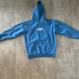 Blå hoodie FSBN Chaotic System M - Blå hoodie från FSBN i relaxed fit med vit Chaotic System-tryck på bröstet. Tröjan har huva, magficka och vita kontrastdetaljer längs ärmarna. Tillverkad i mjuk bomull, perfekt för chill dagar. Storlek M.