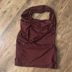 Vinröd multifunktionell topp - Säljer en vinröd topp i mjukt stretchigt material som kan stylas på flera olika sätt – som halterneck, offshoulder eller oneshoulder. Toppen är tight och croppad, perfekt för dig som gillar att variera din look. Materialet är lent och följsamt, vilket gör den superbekväm. Endast testad, liten i storlek