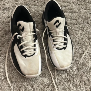 Svarta och vita Nike sneakers - Nike inneskor/basketskor i svart och vitt med snyggt mönstrad sula och klassisk swoosh på sidan. Skorna har snörning och rund tå, tillverkade i syntetmaterial med mesh-paneler för bra ventilation. Perfekt för dig som gillar sportig stil och vill ha bekväma skor med cool design.