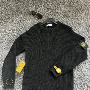 Stone Island tröja  - Säljer en svart stickad tröja från Stone Island med klassisk rund hals och ikonisk patch på vänster ärm. Tröjan har en grovstickad struktur och långa ärmar, perfekt för dig som gillar streetwear och vill ha en clean look. Storlek är L men passar bäst till M 