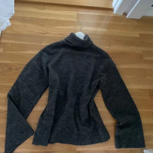 Mörkgrå stickad polotröja - Mysig mörkgrå stickad polotröja med ribbad krage och muddar. Perfekt för kyliga dagar och enkel att matcha med jeans eller kjol. Tröjan har en klassisk passform och är riktigt skön att ha på sig.