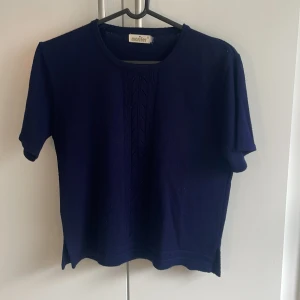 Mörkblå stickad topp från Marifer - Mörkblå stickad topp från Marifer med korta ärmar och rund hals. Framsidan har ett diskret stickat mönster som ger en snygg detalj. Perfekt till jeans eller kjol för en chill och stilren look.