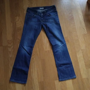 Lee jeans - Snygga blå jeans från Lee i modellen CADE, med klassisk bootcut och låg midja. Jeansen har fem fickor och dubbla knappar i midjan. Bra skick.