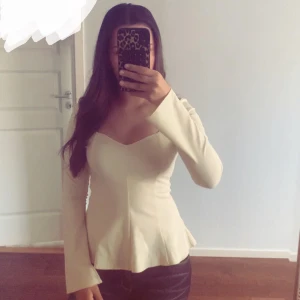 Ljus gul långärmad blus med v-ringning - Säljer en stilren beige blus med lång ärm och v-ringad hals. Toppen har figurnära passform upptill och lätt utsvängd nertill för en snygg siluett. Perfekt att matcha med jeans eller kjol för en trendig look.