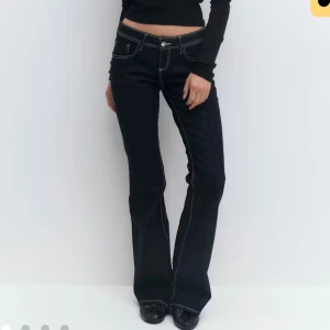 Mörkblå flare jeans med kontrastsömmar - Snygga mörkblå jeans med vita kontrastsömmar och flare-modell. Låg midja och klassisk femficksdesign. Perfekta för dig som gillar en retro vibe och vill sticka ut med detaljer. Tillverkade i jeansmaterial.