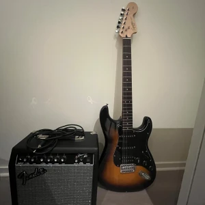 Fender Squier Stratocaster med Fender Frontman 15G förstärkare - Säljer en Fender Squier Stratocaster elgitarr i sunburst med tillhörande Fender Frontman 15G förstärkare och original gitarrväska. Allt i fint skick, perfekt för både nybörjare och erfarna musiker. Kabel  medföljer.