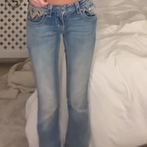 Lågmidjade miss me jeans - Snygga ljusblå jeans med coola mönstrade detaljer på fickorna. Låg midja och W25. Skulle säga raka men de går ut lite. Pärlorna där bak har åkt av lite därmed kan pris diskuteras❤️