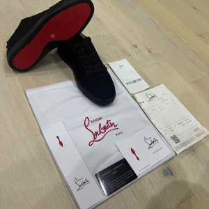 Svarta sneakers från Christian Louboutin - Snygga svarta sneakers från Christian Louboutin med den ikoniska röda sulan. Skorna har snörning och en stilren design i svart med rund tå. Tillverkade i skinn och textil, levereras med dustbag och äkthetskort. Pris kan diskuteras!!