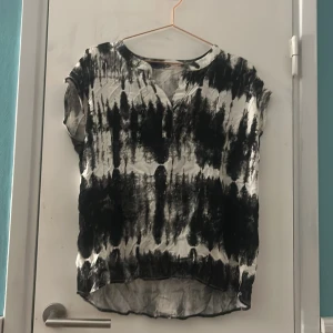 Svartvit blus med abstrakt mönster - Säljer en cool svartvit blus med abstrakt mönster. Blusen har korta ärmar och rund halsringning med liten v-ringad öppning. Materialet känns lätt och luftigt, perfekt för dig som gillar en unik stil. Passar dig som vill sticka ut med en konstnärlig vibe. Vet ej storlek men gissar på M/L