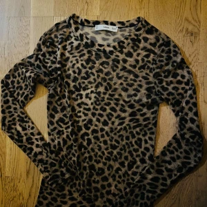 Leopardmönstrad meshtröja från MNG - Säljer en tunn och stretchig långärmad meshtröja från MNG med leopardmönster i beige och svart. Tröjan har rund halsringning och sitter snyggt tight mot kroppen. Perfekt för dig som gillar djurmönster och vill sticka ut.