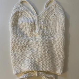 Handvirkad topp - Superfin handvirkad topp i vit färg med croppad passform. Toppen har smala axelband och snygg snörning i ryggen. Stickad struktur och mjukt material gör den perfekt för varma dagar. 