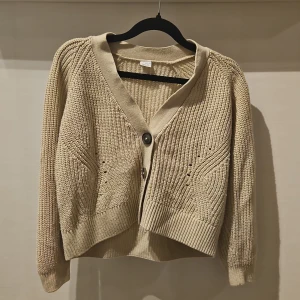 Beige stickad kofta från Lindex stl 146/152 - Snygg beige stickad kofta från Lindex med coola detaljer i stickningen och tre stora knappar framtill. Koftan har långärmad passform, ribbade muddar och v-ringad hals. Perfekt för dig som gillar chill och stilren look.