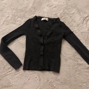 Mörkgrå ribbad kofta från Pull&Bear - Snygg mörkgrå ribbad kofta från Pull&Bear i storlek M. Koftan knappar framtill och långa ärmar. Den är stretchig och mjuk, den ser ganska liten ut men den stretchas ut när man sätter på den. 