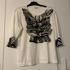 Vit blus med zebramönstrade volanger - Säljer en vit blus från Esmara med coola zebramönstrade volanger framtill och på ärmsluten. Blusen har trekvartsärm och rund halsringning. Materialet känns mjukt och luftigt, perfekt för dig som gillar unika detaljer och djurmönster.