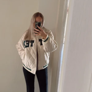 Beige bomberjacka från FB Sister XL - Säljer en beige bomberjacka från FB Sister i storlek XL. Jackan har tryckknappar framtill och stora bokstäver på bröstet. Den har en loose passform och är perfekt för dig som gillar sportig och trendig stil.